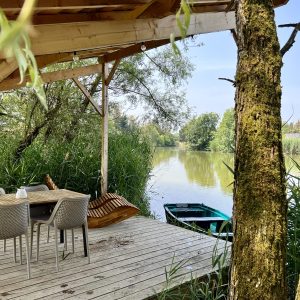 Cabane sur pilotis avec terrasse surplombant un paisible plan deau entouré de verdure.