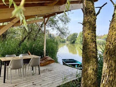 Hébergement insolite : terrasse en bois au bord de l'eau, entourée de verdure et d'un canoë.