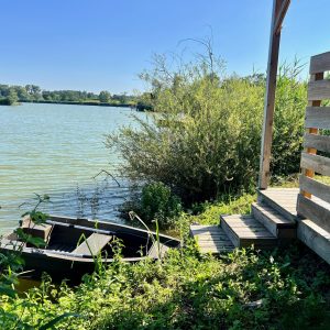 Cabane au bord de l'eau, avec un petit bateau amarré et une vue sur la nature verdoyante.