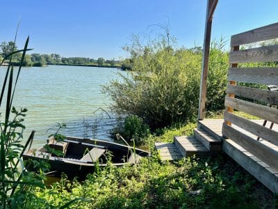 Cabane au bord de l'eau, avec un petit bateau amarré et une vue sur la nature verdoyante.