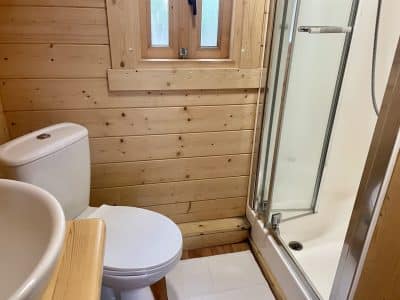 Salle de bain en bois dans un hébergement insolite, avec douche et toilettes modernes.