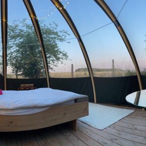 Cabane en verre avec lit douillet et vue sur la nature, décor coloré.