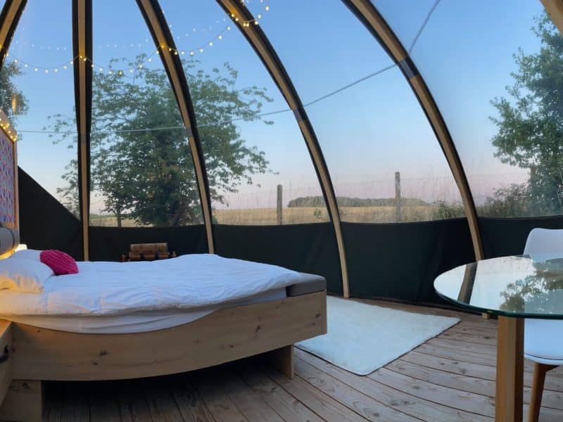 Cabane en verre avec lit douillet et vue sur la nature, décor coloré.
