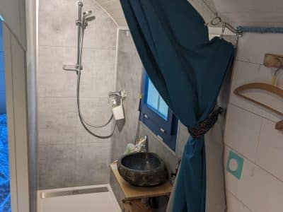 Douche moderne dans un hébergement insolite, avec un lavabo en pierre et des rideaux colorés.