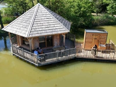 Cabane sur pilotis au bord de l'eau, avec terrasse en bois et vue sur la nature environnante.