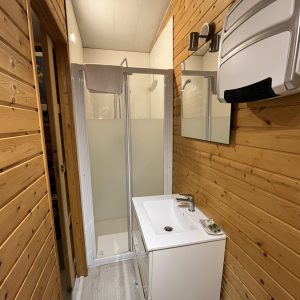 Salle de bain en bois dans un hébergement insolite, avec douche et lavabo moderne.