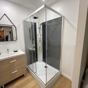 Salle de bain moderne avec douche à l'italienne et meuble en bois clair. Éclairage chaleureux.
