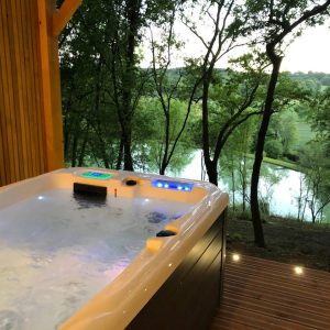 Bain à remous en bois avec vue sur la rivière, idéal pour un séjour relaxant en pleine nature.