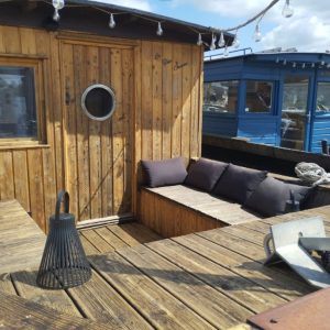 Cabane sur l'eau en bois avec coussins confortables et vue sur la ville, ambiance chaleureuse.