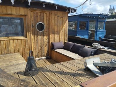 Cabane sur l'eau en bois avec coussins confortables et vue sur la ville, ambiance chaleureuse.