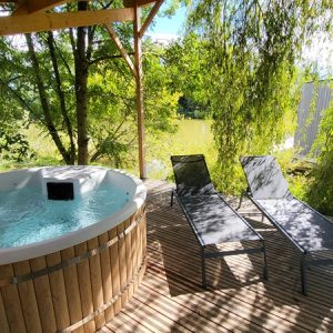 Hébergement insolite avec jacuzzi en bois, chaises longues sous un auvent verdoyant.