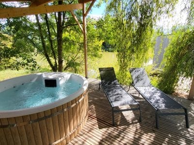 Hébergement insolite avec jacuzzi en bois, chaises longues sous un auvent verdoyant.