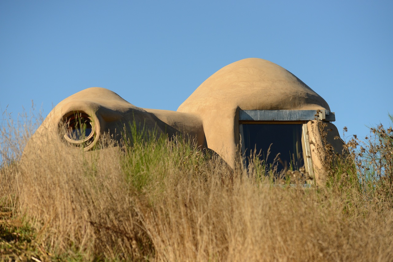 Hébergement insolite en forme de dôme, entouré de végétation sauvage.