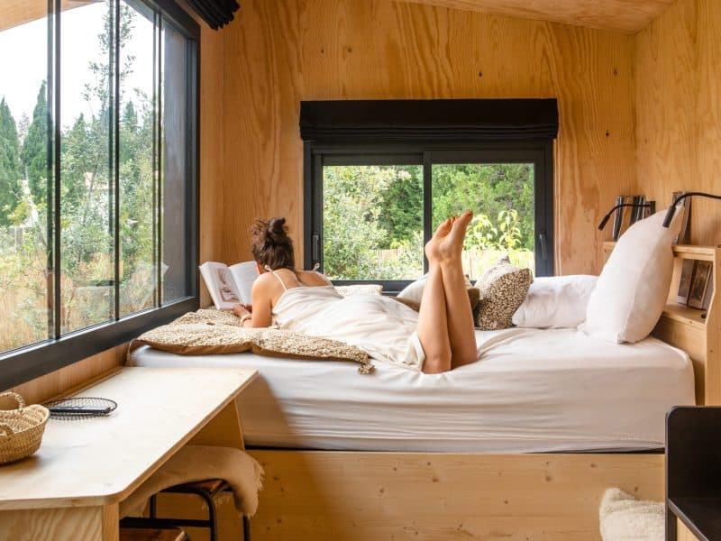 Cabane moderne avec grandes fenêtres, lit confortable et vue sur la nature.