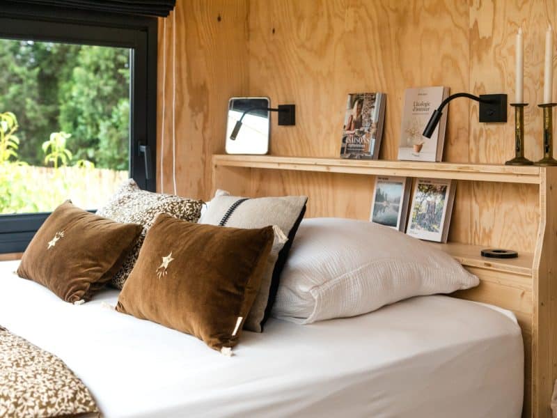 Chambre cosy en bois avec lit douillet et coussins élégants, vue sur la nature.
