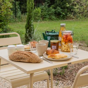 Table de petit-déjeuner en plein air, avec des mets variés et une vue sur la nature verdoyante.