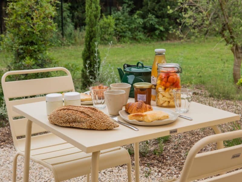 Table de petit-déjeuner en plein air avec des mets frais et un jardin verdoyant.