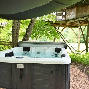 Hébergement insolite : cabane dans les arbres avec jacuzzi en pleine nature, entourée d'arbres.