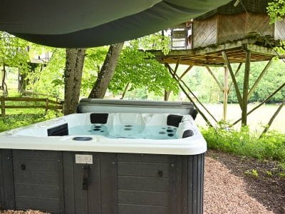 Hébergement insolite : cabane dans les arbres avec jacuzzi en pleine nature, entourée d'arbres.