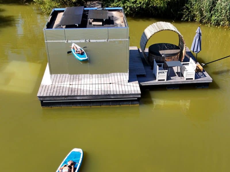 Cabane flottante moderne avec terrasse et kayak sur leau calme.