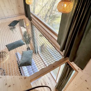 Cabane en bois avec un filet suspendu, baignée de lumière naturelle et vue sur la nature.