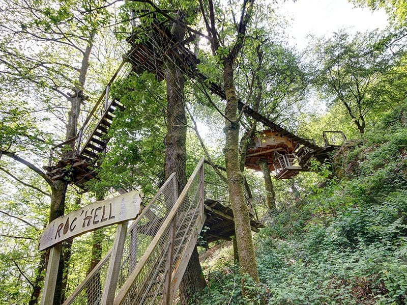 Cabane perchée dans les arbres, entourée de verdure, offrant une vue imprenable.