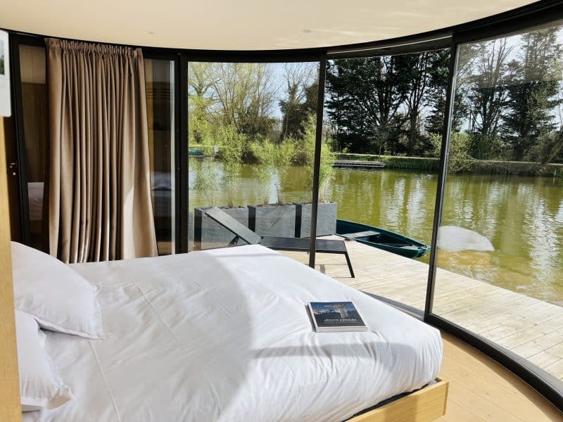 Chambre moderne en rond, vue sur un lac paisible, baignée de lumière naturelle.