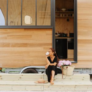 Tiny house en bois avec grande baie vitrée, terrasse accueillante et fleurs en pot.