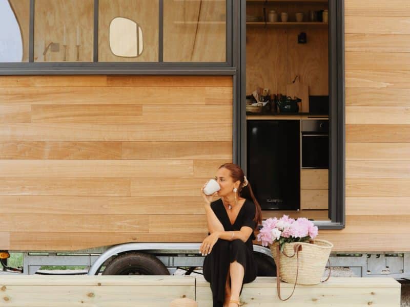 Cabane en bois avec terrasse, une femme sirotant un café devant lentrée.