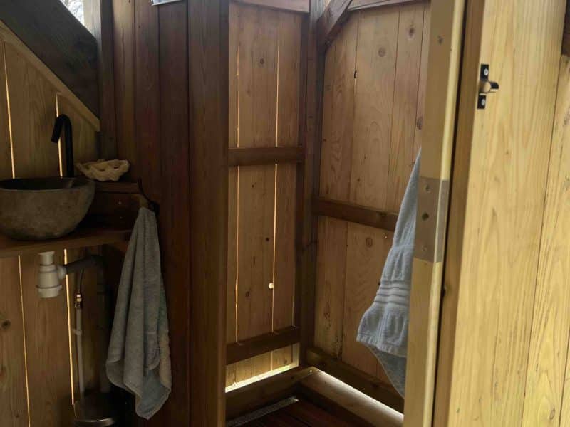 Douche extérieure en bois dans un hébergement écologique, ambiance naturelle et chaleureuse.