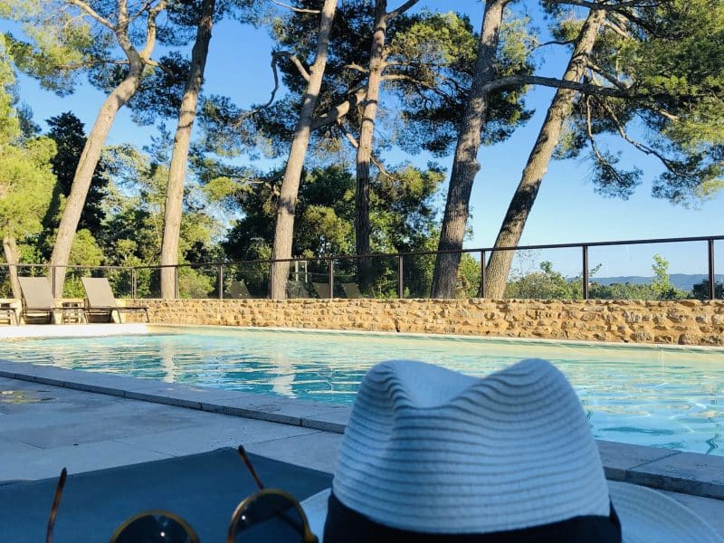 Villa avec piscine, chapeau et lunettes de soleil au bord de leau, entourée darbres.