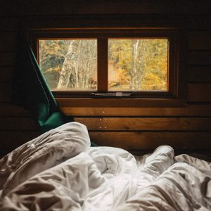 Chalet cosy avec vue sur la nature, draps blancs en désordre et lumière douce.