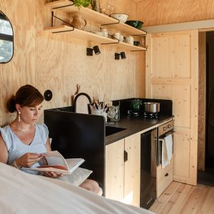 Tiny house en bois clair, avec cuisine équipée et coin lecture confortable.
