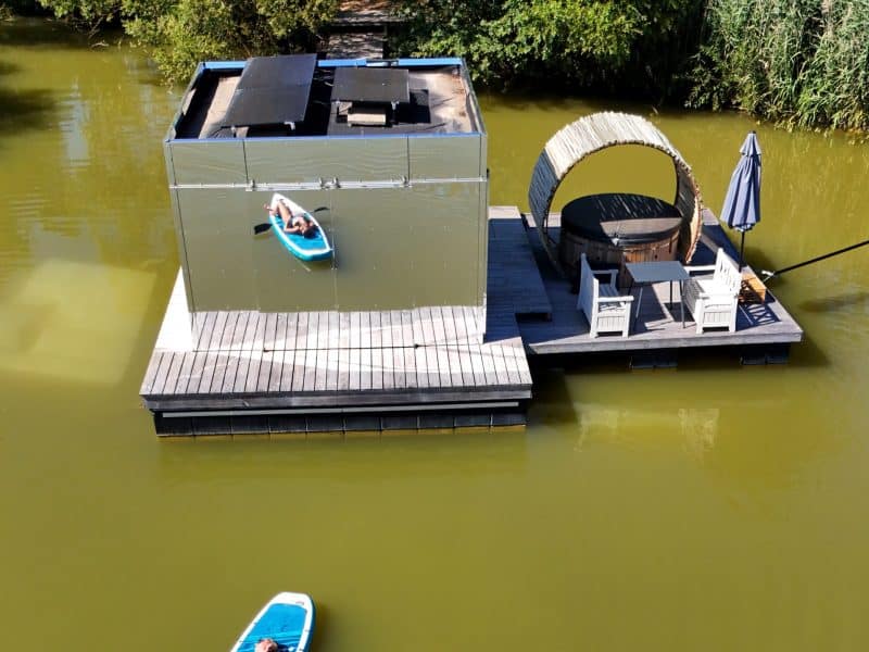 Cabane flottante moderne sur un lac, avec un espace détente et kayak à proximité.