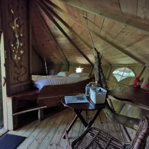 Cabane perchée en bois, avec un lit douillet et des lanternes, au cœur des arbres.