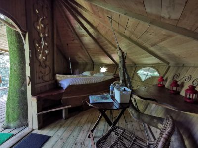 Cabane perchée en bois, avec un lit douillet et des lanternes, au cœur des arbres.