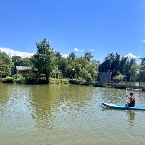 Canoë sur un lac paisible, entouré de verdure et de cabanes en bois. Évasion nature garantie.