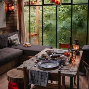 Un chalet en bois avec une table dressée, baigné de lumière naturelle et verdure environnante.