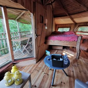 Cabane perchée en bois, lit douillet à baldaquin, vue sur la nature verdoyante.
