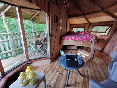 Cabane perchée en bois, lit douillet à baldaquin, vue sur la nature verdoyante.