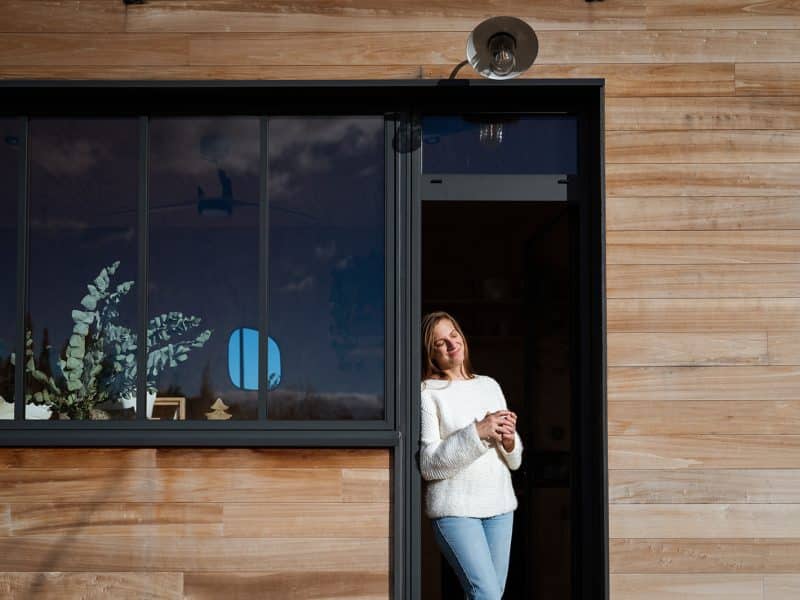Chalet moderne en bois avec une femme souriante tenant une tasse à café.