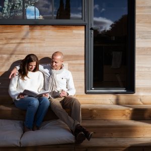 Un chalet en bois moderne, couple détendu sur des marches, profitant du soleil.