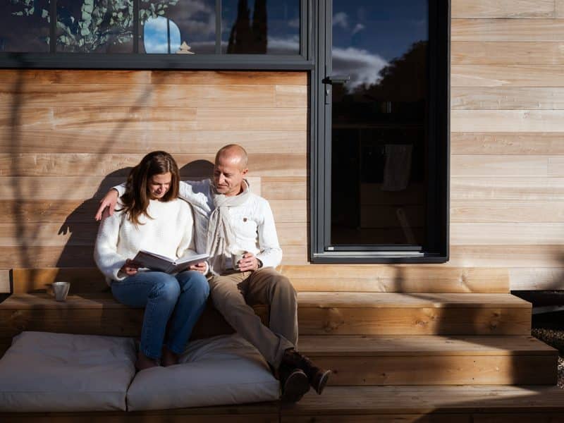 Cabane en bois moderne avec un couple détendu sur une terrasse ensoleillée.