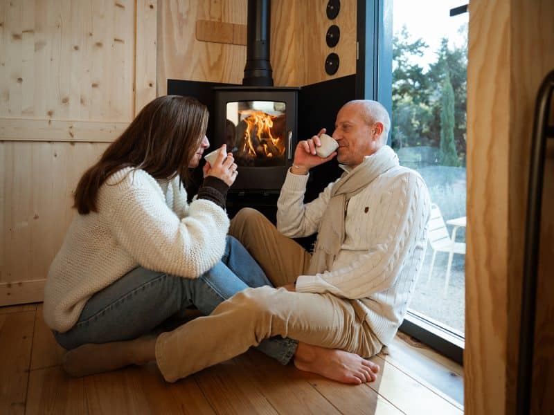 Cabane chaleureuse avec poêle à bois, couple savourant des boissons chaudes.