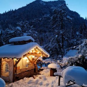 Chalet en bois sous la neige, illuminé par des guirlandes, entouré de montagnes.
