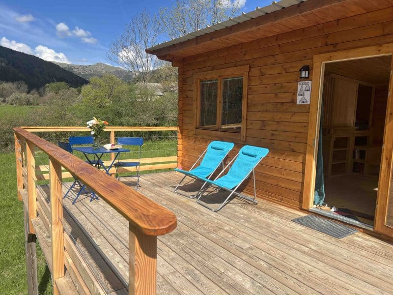 Charmante cabane en bois avec terrasse ensoleillée et chaises longues.