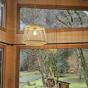 Cabane en bois avec lampes suspendues, vue sur un jardin verdoyant et un petit lac.