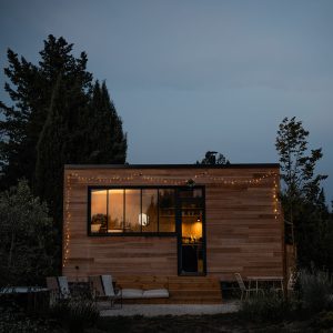 Cabane en bois avec guirlandes lumineuses, entourée d'arbres, créant une ambiance chaleureuse.