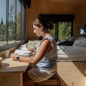 Cabane en bois avec grandes fenêtres, offrant une vue sur la nature et un coin lecture cosy.