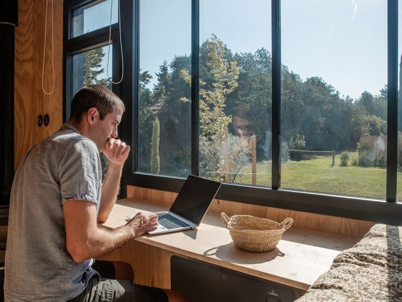 Tiny house moderne avec grande fenêtre, vue sur la nature et espace de travail confortable.